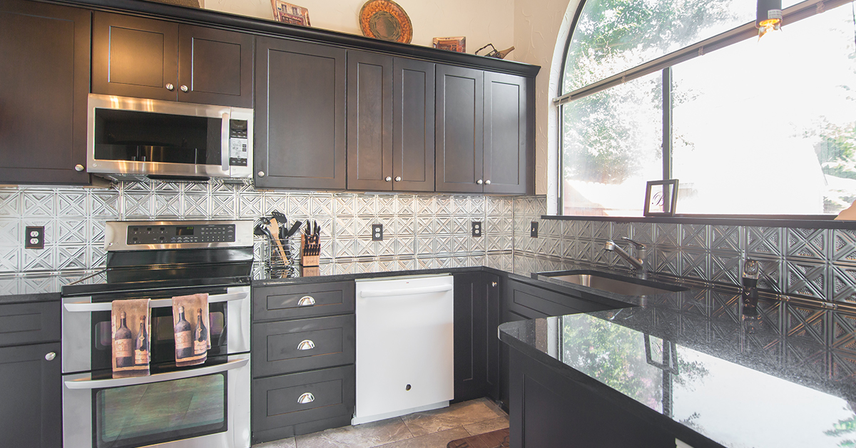 Kitchen with dark cabinets and countertop and silver tin tile backsplash.