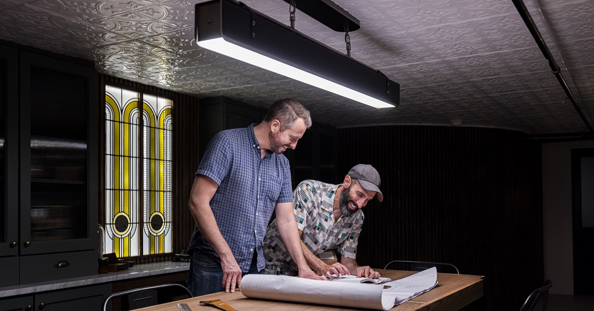 Barry and Jordan look over blueprints for a project in their basement with stained glass window feature behind them.