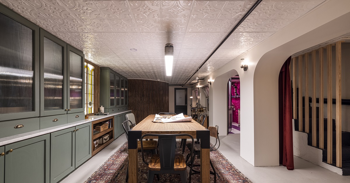 Long shot of the finished basement with green cabinetry, white ceilings, and a long wood table in the center of the room.